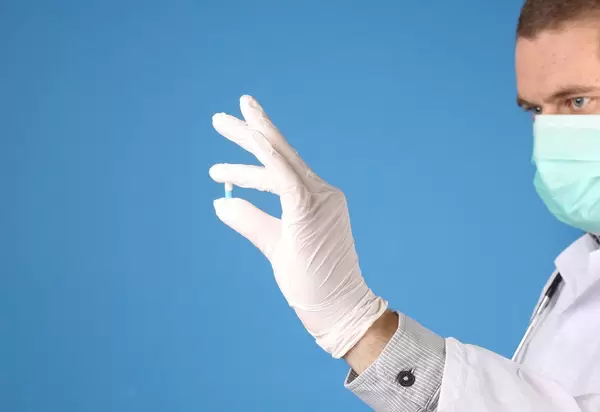 Doctor holding small pill on blue background