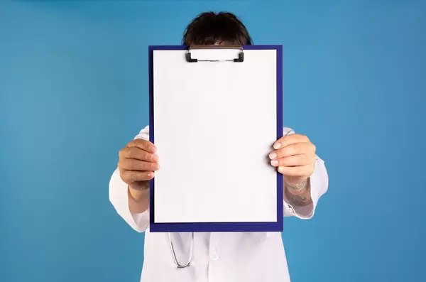 Doctor showing blank clipboard on blue background