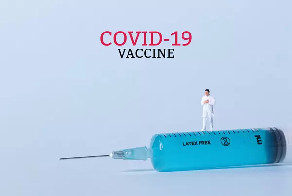 Doctor standing on a syringe and Covid-19 vaccine text