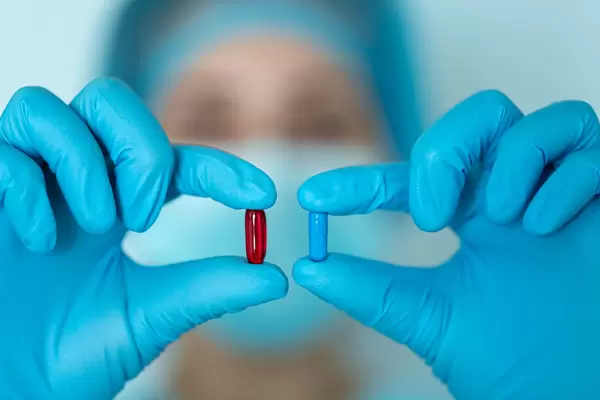 Doctor's hands in blue latex glove hold red and blue medical capsules
