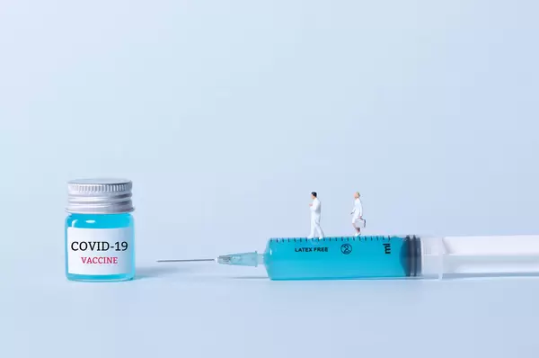 Doctors standing on a syringe and bottle with blue fluid and Covid-19 Vaccine text