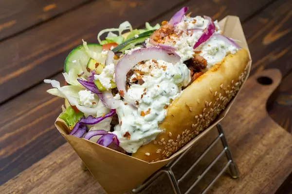 Döner Kebab mit gemischtem Fleisch, frischen Gemüse, Tzatziki, Feta Käse und Chili in frischem Brot auf einem Holzbrett Nahaufnahme