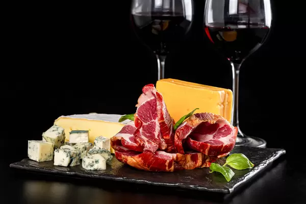 Dor Blue, brie, Dutch cheese, ham on a black background with two glasses of wine