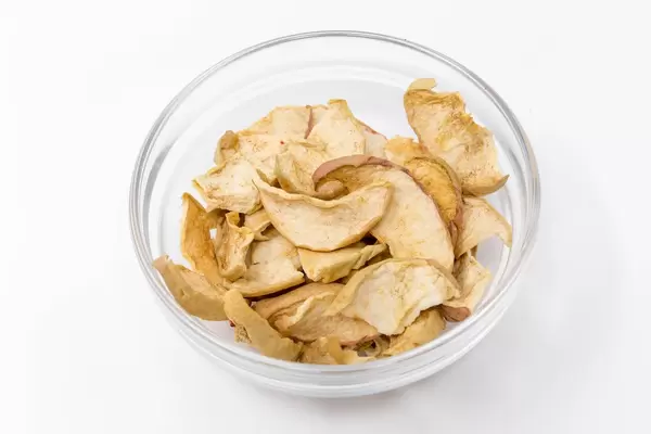 Dörrwerk - Getrocknete Apfel Chips mit Zimt in Glaschale auf weißem Hintergrund