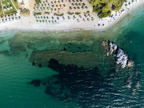 Draufsicht: der Strand Milia auf Skopelos mit türkisem Wasser und Stroh- und blau-gelben Sonnenschirmen