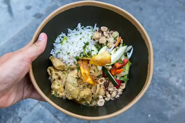 Draufsicht: Hand hält einen schwarzen tiefen Teller mit Curry-Landhuhn, Gemüse und Reis. Q11, Pollença