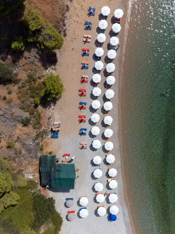 Draufsicht: Kokkinokastro Strand auf Alonnisos mit Reihen von weißen Sonnenschirmen
