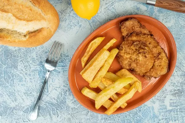 Draufsicht von Hähnchen Schnitzel mit Pommes auf einem Teller mit Brötchen und Zitrone