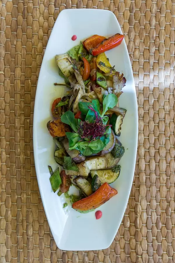 Draufsicht von langem Teller mit gegrilltem Sommergemüse, frischen Pilzen und Avocadocreme