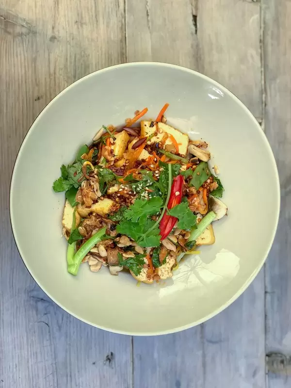 Draufsicht von PHO XAO SOT ME. Bio-tofu in Streifen gebraten mit Bandnudeln, Zwiebeln, Möhren, Buschbohnen, Shiitake-pilzen, Tamarindesauce, Sesam, Erdnüsse, Röstzwiebeln