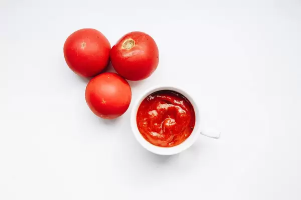Draufsicht von Tomatensoße in einer Tasse und Tomaten drumherum. Weißer Hintergrund