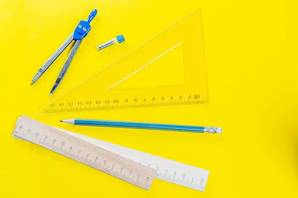 Drawing kit-ruler, compass and pencil on yellow background