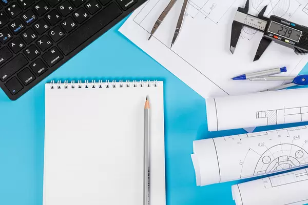 Drawings and project engineering work with keyboard, pencils and notepad on a blue background