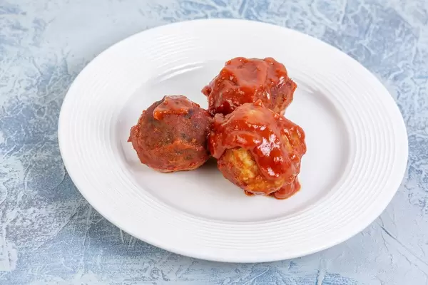 Drei Hackbällchen mit Tomatensoße auf weißem Teller auf Marmortisch