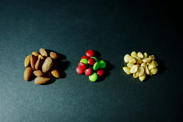 Drei Haufen mit Mandeln, bunten Süßigkeiten und geschälten Erdnüssen auf dunklem Untergrund
