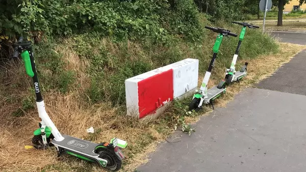 Drei Lime Elektroroller im Gras geparkt auf einer Straße von München