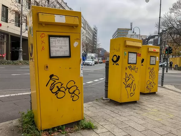 Drei mit Graffiti bemalte, gelbe Briefkästen der Deutschen Post an Straßenkreuzung