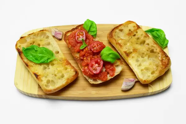 Drei Panini mit Knoblauch und Tomate auf Holzbrett, dekoriert mit Basilikum, Cherrytomaten und Knoblauchzehe