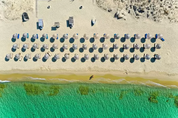 Drei Reihen Strandliegen mit Sonnenschirmen am schönen Strand von Plaka auf Naxos. Luftaufnahme