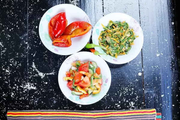 Drei Salatschüsseln auf einem schwarzen Hintergrund, Aufnahme von oben: eingelegte Paprika, frisches Gemüse-Mix und Karottensalat