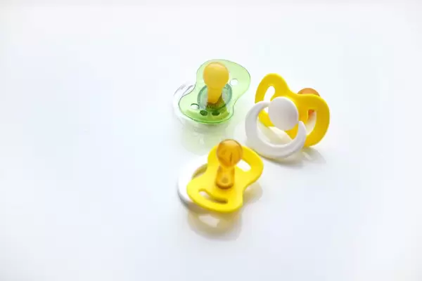 Drei Schnuller in gelb-weiß und transparentem grün vor weißem Hintergrund