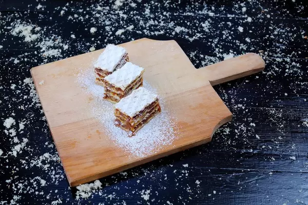 Drei Stück hausgemachter Karamellkuchen auf einem Holzbrett vor einem schwarzen Hintergrund