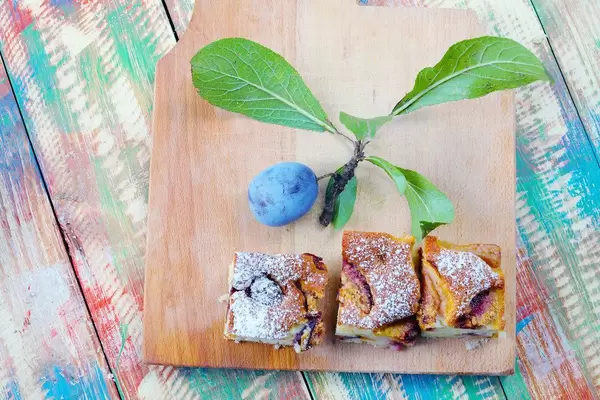 Drei Stück Pflaumenkuchen mit einer frischen Pflaume auf einem Holzbrett