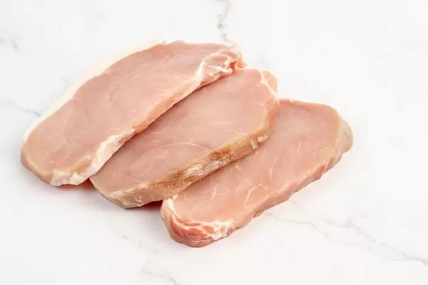 Drei Stück rohes Schweinefleisch nebeneinander, auf einer marmorierten Oberfläche