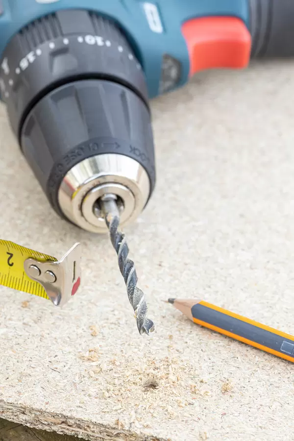 Drilled hole on the plywood with tape measure drill and pencil