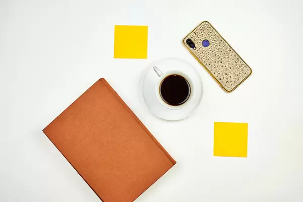 Drinking refreshing coffee at a bright workplace with a notebook, sticky notes, and smartphone