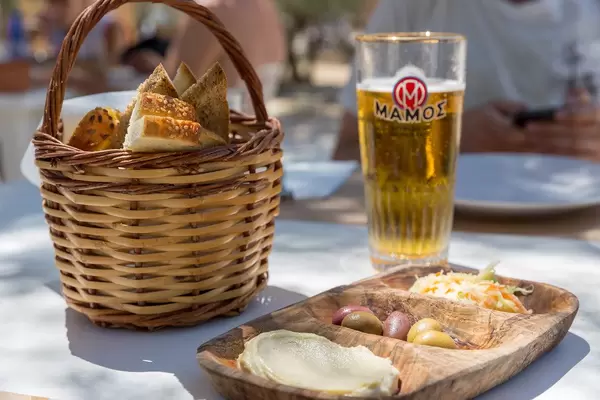 Drinks and a bread basket, next to Mediterranean food, like humus and olives, in a Greek restaurant on Paros Island