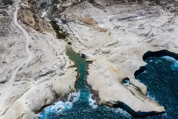 Drohnenaufnahme an der griechischen Küste auf Milos mit weißen Klippen, kleiner Bucht, rauem Meer