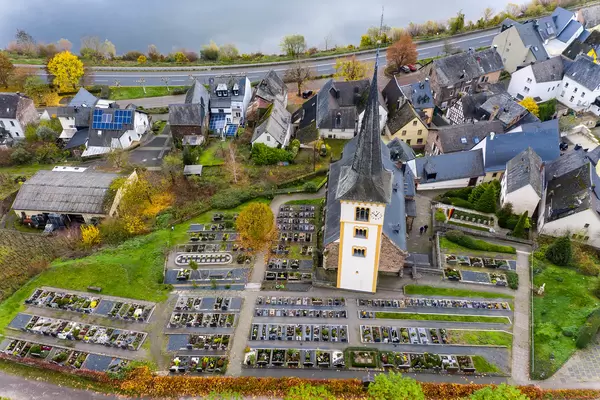 Drohnenaufnahme der St. Laurentius Kirche mit Parkplatz und Häusern an dem Fluss Mosel in Bremm, Deutschland