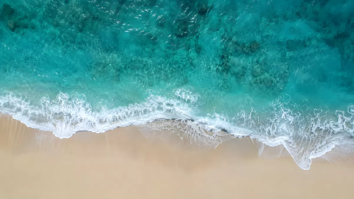 Drohnenaufnahme türkisfarbenes Meer trifft Sandstrand