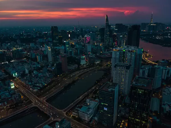 Drohnenaufnahme vom Stadtzentrum mit Bitexco Financial Tower, anderen Hochhäusern und Saigon River mit Landmark 81 im Hintergrund bei Nacht in Ho Chi Minh Stadt, Vietnam