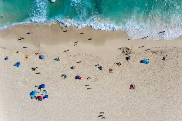 Drohnenaufnahme vom Strand Cala Mesquida auf Mallorca mit Wellen, Sand und Touristen