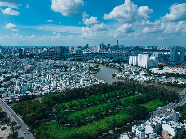 Drohnenaufnahme von einem öffentlichen Park neben dem Saigon Fluss in Distrikt 8 und der Skyline mit Bitexco Financial Tower und Landmark 81 in Ho Chi Minh Stadt, Vietnam