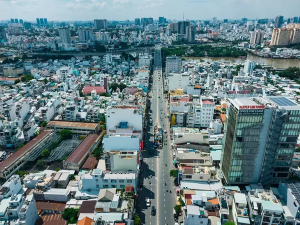 Drohnenaufnahme von Häusern, Bürogebäude, Kirche und einer Schule entlang einer Straße in Distrikt 8 welche zu einer Brücke über den Saigon Fluss führt in Ho Chi Minh City, Vietnam
