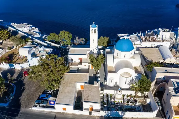 Drohnenaufnahme. Weiße Kirche und Glockenturm mit blauen Kuppeln und Friedhof auf Santorin