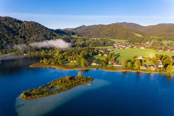 Drohnenfoto der Stadt Ringsee am Ufer des Tegernsees mit kristallklarem Wasser und einer kleinen Insel am See