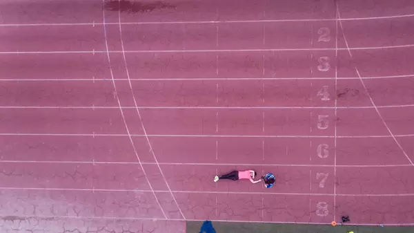 Drohnenfoto einer erschöpften Läuferin, die auf der Laufbahn liegt