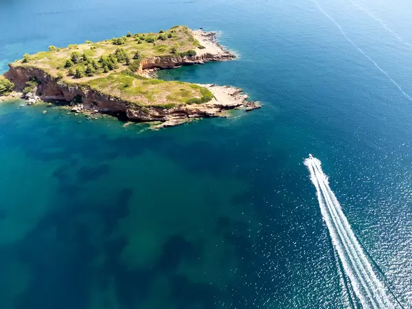 Drone photo: a motorboat skirts the jagged coastline of Kokkinonisi ("Red Island") in front of Kokkinokastro