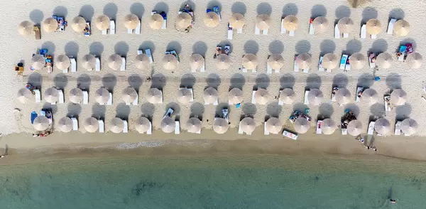 Drone photo: four rows of sun umbrellas in tropical style on the beach of Greek island Tsoungria