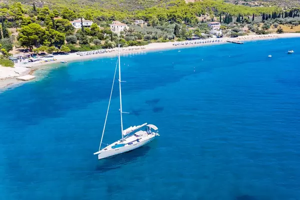Drone picture of a sailboat on the clear blue Myrtonic Sea, with Spetses Island in the background
