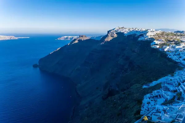 Drone shot: the volcanic cliffs of Santorini, the sea and the capital of the island, Firá in blue light