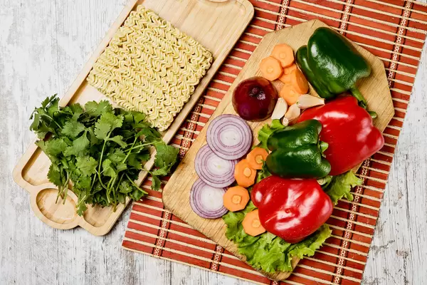 Dry quick cooking noodles and pile of fresh vegetable on the cutting board