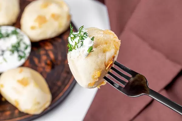 Dumpling with cabbage on a fork with sour cream and dill (Flip 2020)