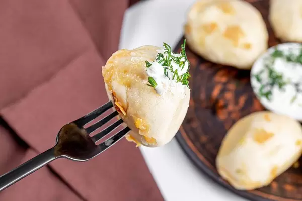 Dumpling with cabbage on a fork with sour cream and dill