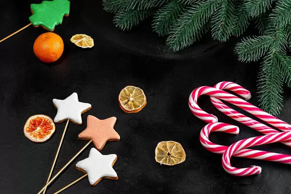 Dunkler Weihnachtshintergrund mit Lebkuchen, Mandarinen und Zuckerstangen
