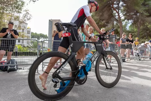Dynamische Quersicht - Ein Sportler mit Nummer 112 besteigt sein Rad beim Challenge Triathlon in Peguera